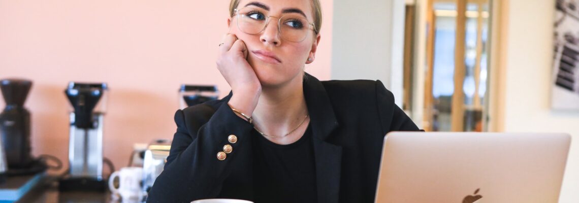 Distracted woman sitting at desk with laptop and coffee cup
